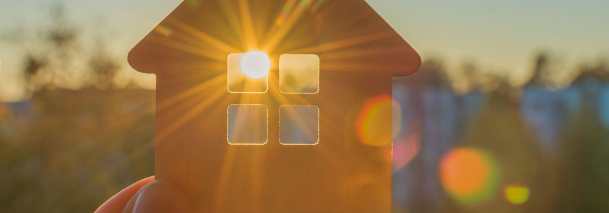 Klein huisje waar zon door raam schijnt. Afbeelding wordt gebruikt om energieopwekking uit zonnecellen in ramen te verbeelden.