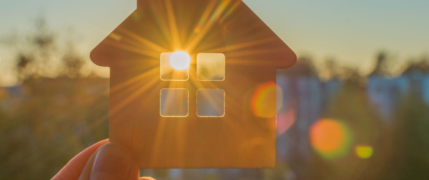 Klein huisje waar zon door raam schijnt. Afbeelding wordt gebruikt om energieopwekking uit zonnecellen in ramen te verbeelden.