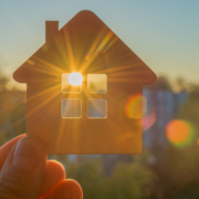 Klein huisje waar zon door raam schijnt. Afbeelding wordt gebruikt om energieopwekking uit zonnecellen in ramen te verbeelden.