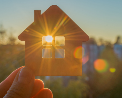 Klein huisje waar zon door raam schijnt. Afbeelding wordt gebruikt om energieopwekking uit zonnecellen in ramen te verbeelden.